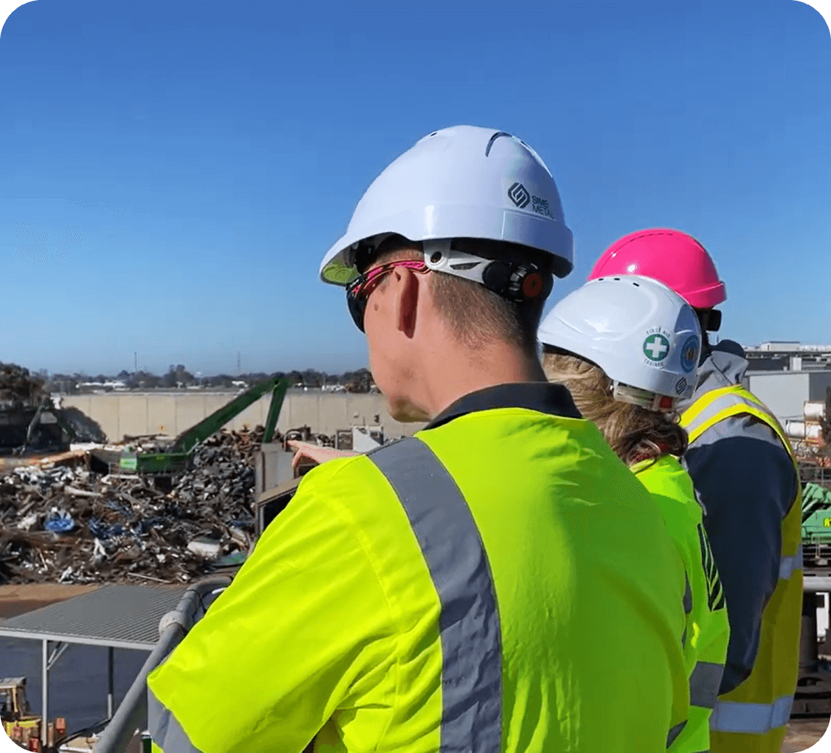 Sims employees in safety gear observing an outdoor scrap metal recycling yard from a high vantage point
